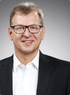 Foto von Armin Vilinger, Porträt eines Mannes mit Bart und Brille, lächelnd, vor einem neutralen Hintergrund.