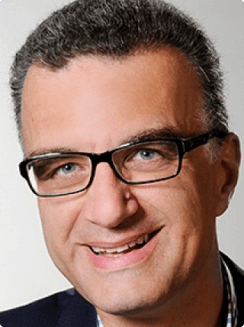 Foto von Guido Grewe, Porträt eines Mannes mit kurzen Haaren und Brille, lächelnd, vor einem neutralen Hintergrund.