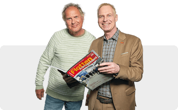 Zwei Männer stehen zusammen, einer hält eine Zeitschrift mit dem Titel „IFL Science Management“ in der Hand, auf deren Titelseite ein Baufahrzeug abgebildet ist. Beide schauen in die Kamera und lächeln.
